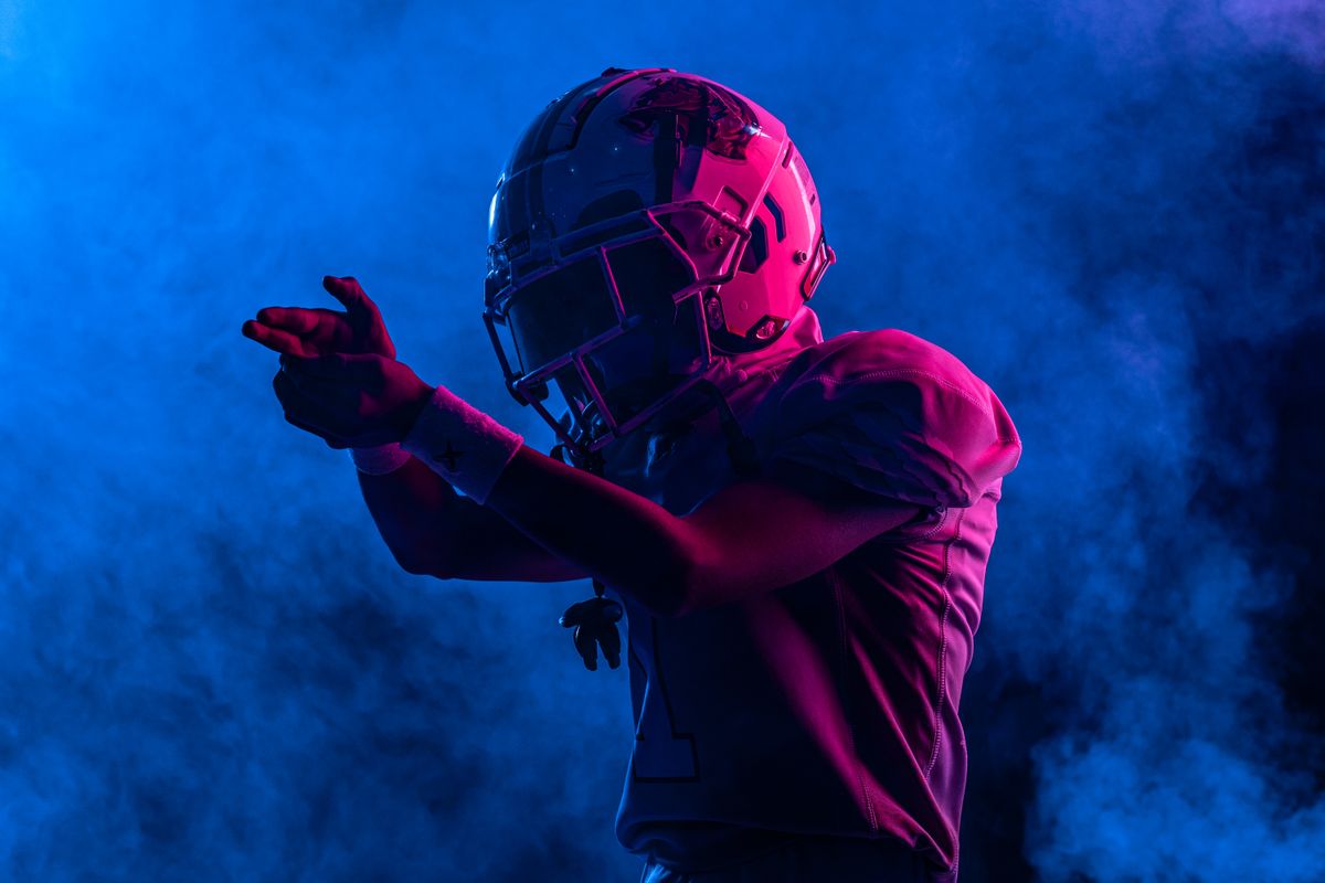 A football helmet in dramatic red and blue light, face obscured, amid stage smoke